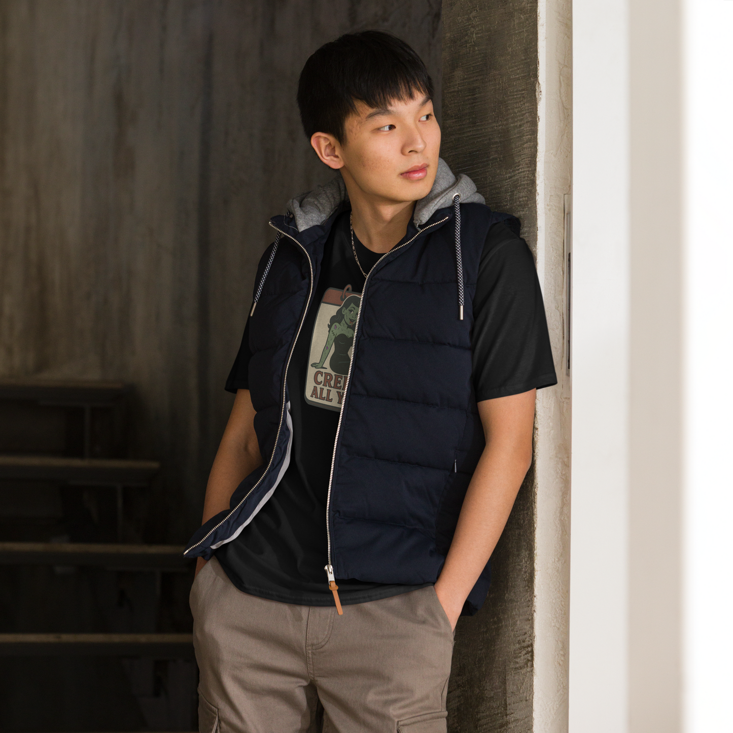 A man indoors standing in front of stairs with black hair wearing cargo pants and t-shirt with vintage style design. The design on the front features a green pinup-style zombie girl holding flowers, with a banner underneath that reads “CREEPY ALL YEAR.”