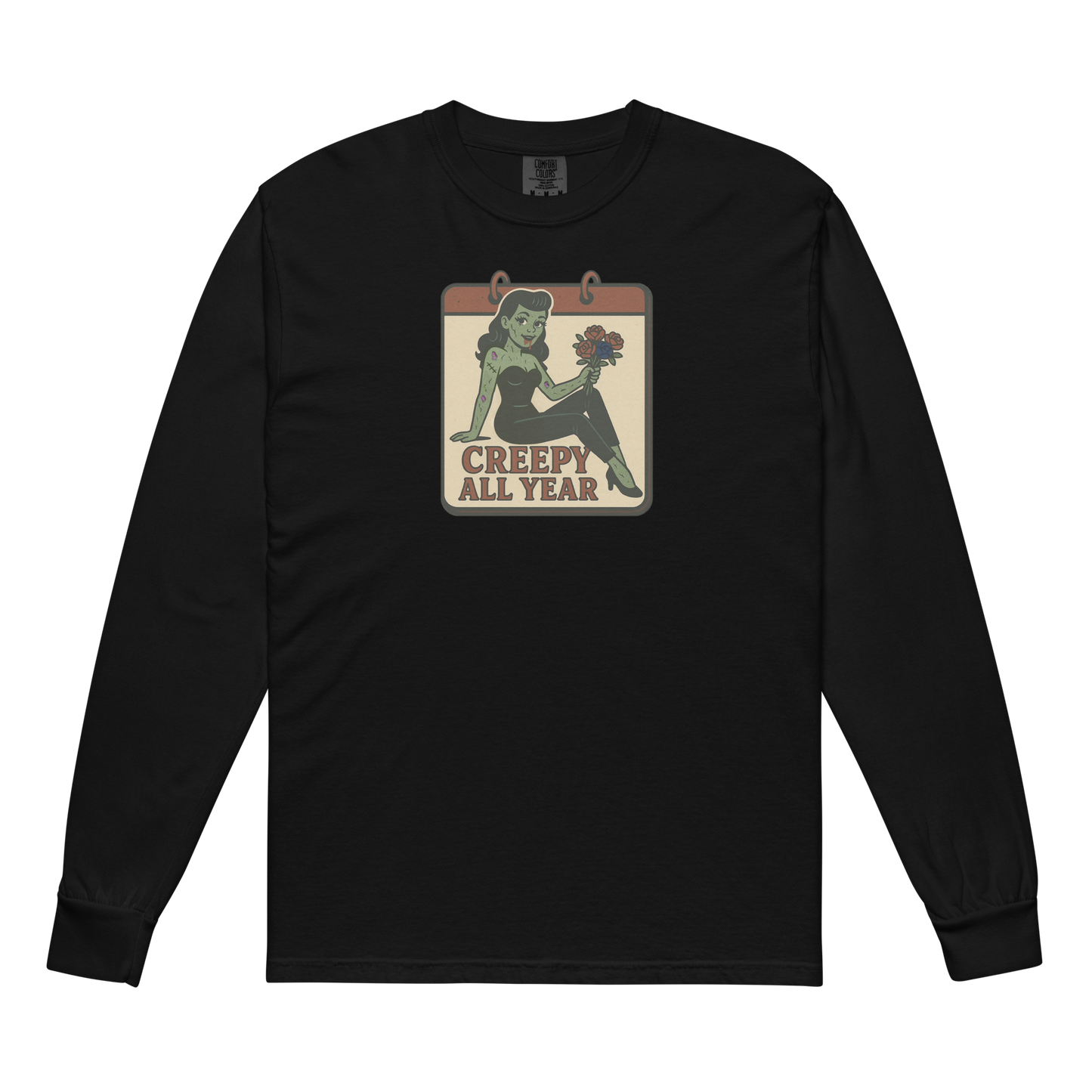 A black long sleeve t-shirt. The design features a green pinup-style zombie girl holding flowers, with a banner underneath that reads “CREEPY ALL YEAR.”