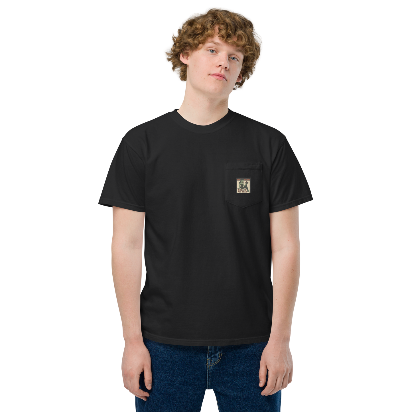White male with light brown hair wearing a black t-shirt with a small vintage-style patch on the pocket area. The patch features a green pinup-style zombie girl holding flowers, with a banner underneath that reads “CREEPY ALL YEAR.”