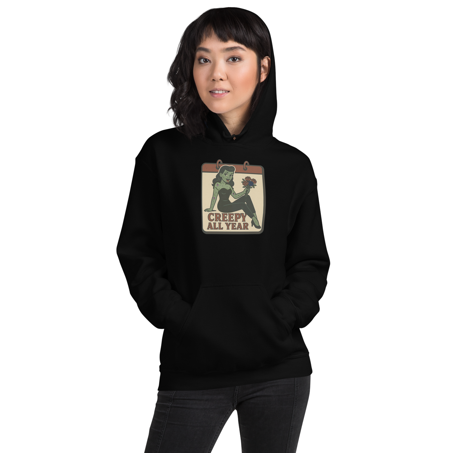 A black hoodie on a girl with shirt black hair with a vintage-style design on the front. The design features a green pinup-style zombie girl holding flowers, with a banner underneath that reads “CREEPY ALL YEAR.”