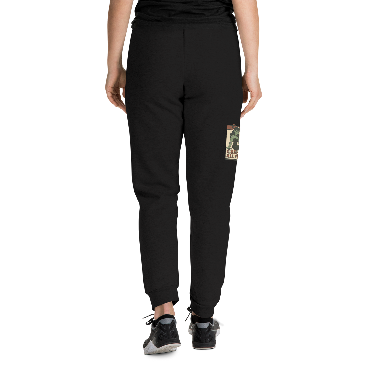 Back of black joggers on a girl with a black t-shirt, with a vintage-style design on the front. The design features a green pinup-style zombie girl holding flowers, with a banner underneath that reads “CREEPY ALL YEAR.”