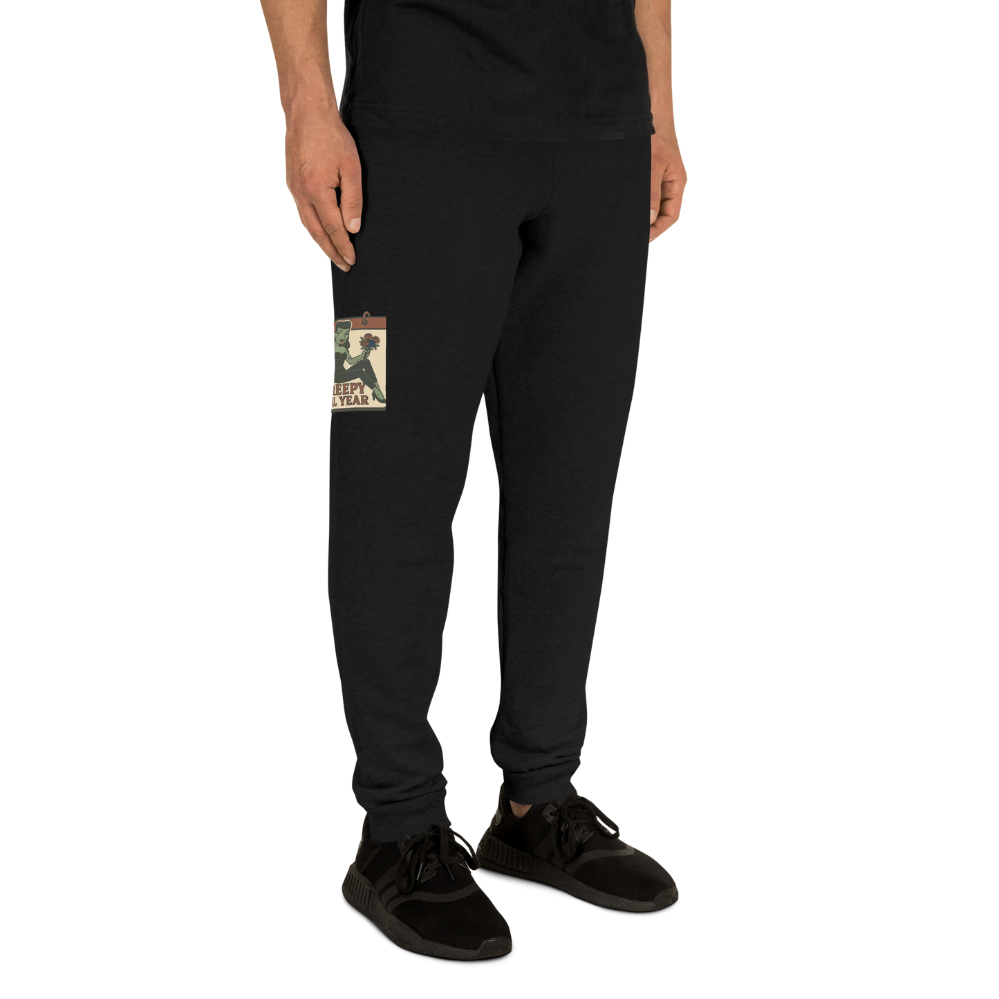 Black joggers on a man with a black t-shirt, with a vintage-style design on the front. The design features a green pinup-style zombie girl holding flowers, with a banner underneath that reads “CREEPY ALL YEAR.”