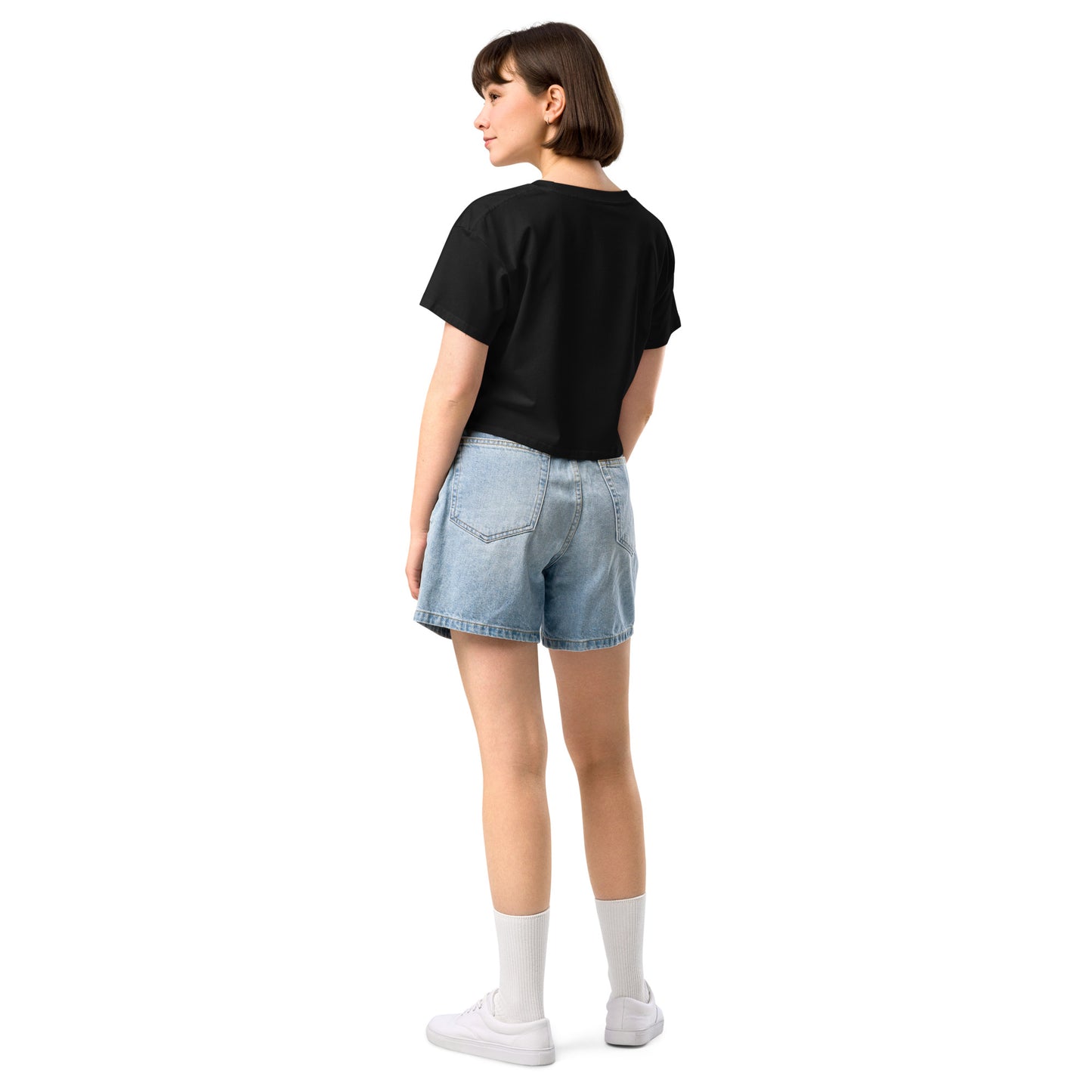 A back of a black crop top on a girl with dark hair with a vintage-style design on the front. The design features a green pinup-style zombie girl holding flowers, with a banner underneath that reads “CREEPY ALL YEAR.”