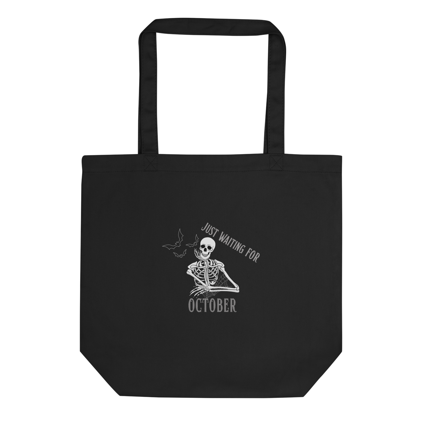 This is a black tote bag that has a bored skeleton with his head resting in his hand and he has spider webs and bats around him and the text reads just waiting for October
