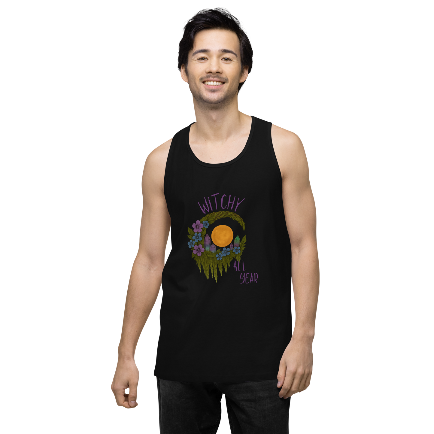 This is a man with dark hair wearing a black tank top with a design of a hand-drawn wreath made of moss-covered branches wraps around a glowing sun. The wreath is decorated with purple and blue flowers, small amethyst and fluorite crystals, and strands of hanging moss. The words “Witchy” curve above the wreath and “All Year” sits on the bottom right