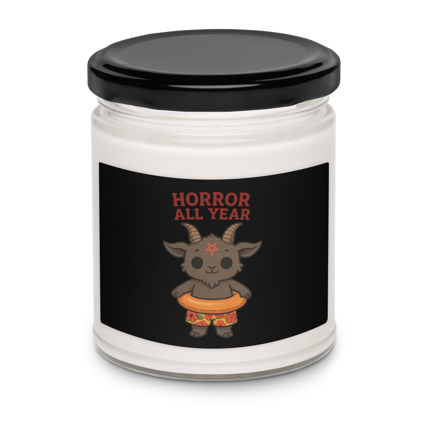 This is a white candle with a black tin lid on top and on the front is a cartoon illustration of a baby Baphomet goat with curved horns and a playful grin, wearing bright floral swim trunks while floating in a colorful inner tube. The character is set against a light background with the bold text “Horror All Year” above in red letters
