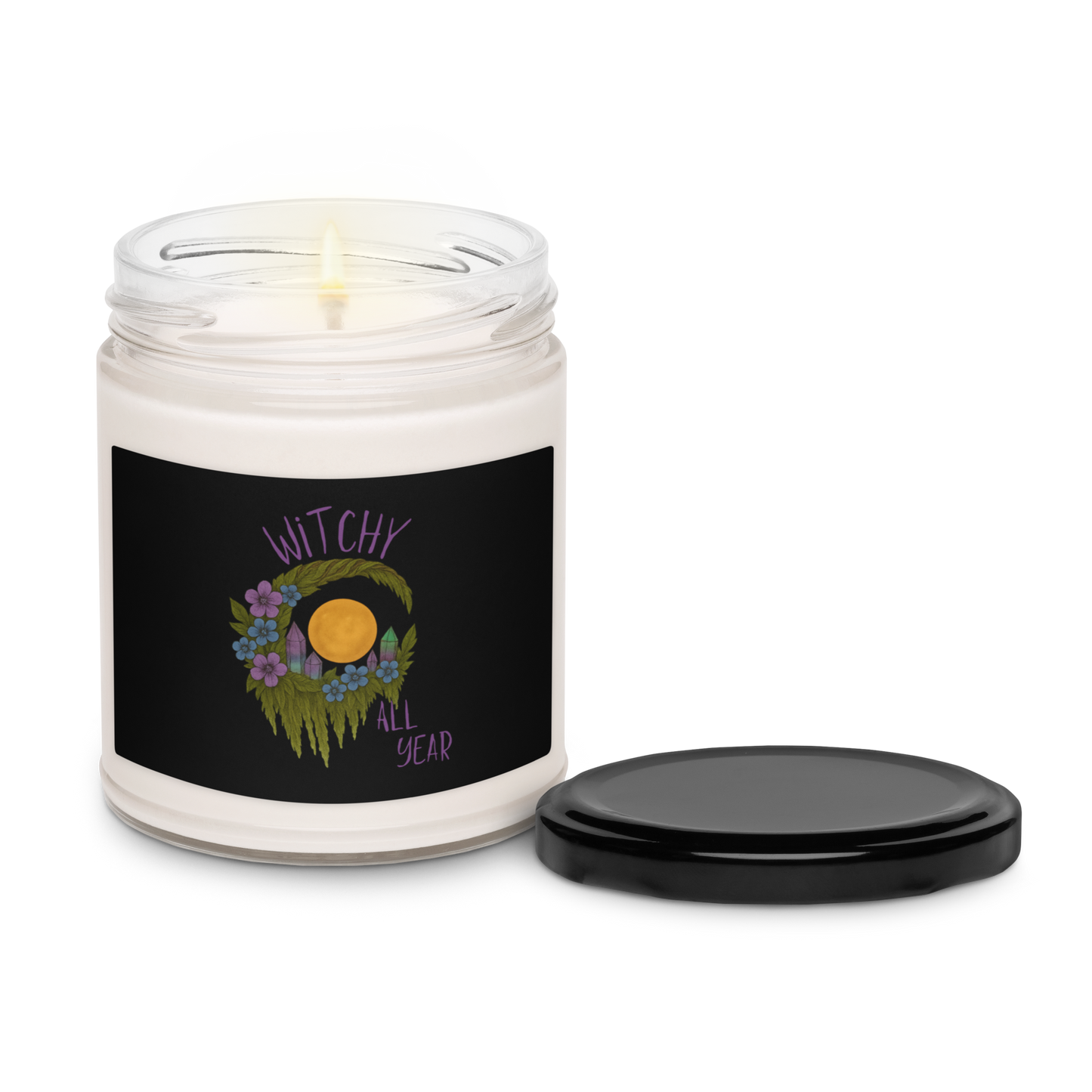 This is a white candle and black tin lid with a design of a hand-drawn wreath made of moss-covered branches wraps around a glowing sun. The wreath is decorated with purple and blue flowers, small amethyst and fluorite crystals, and strands of hanging moss. The words “Witchy” curve above the wreath and “All Year” sits on the bottom right