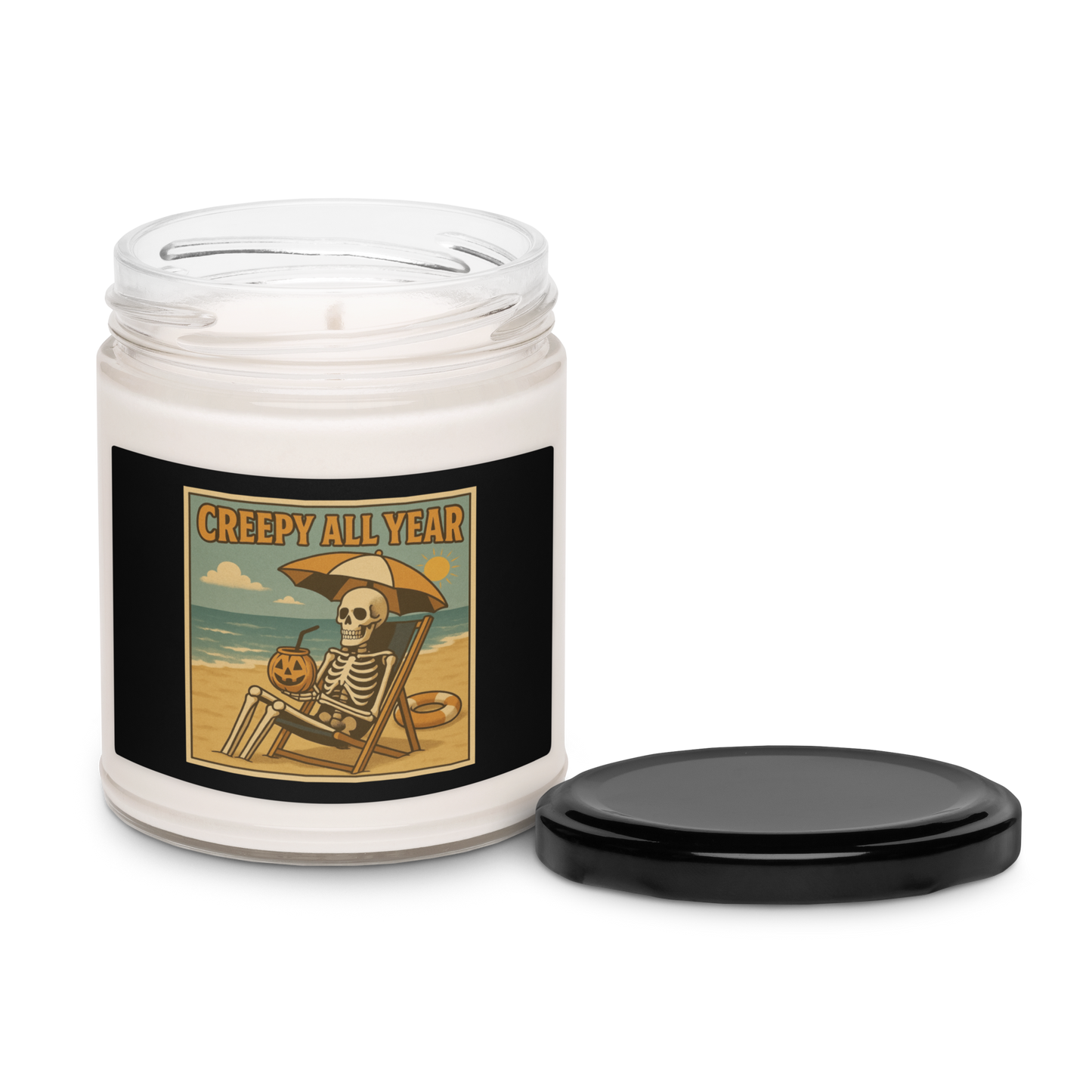 This is a white candle with black tin lid and black label with a retro-style illustration of a grinning skeleton lounging on a beach chair under an orange umbrella. The skeleton is holding a pumpkin-shaped drink cup with a straw and relaxing by the ocean, with a bright sun in the sky and a life preserver in the sand. The words “Creepy All Year” appear boldly at the top