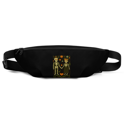 This is a black waist bag with a Día de los Muertos–style illustration of a male and female skeleton holding hands, surrounded by marigolds, vines, and folk art patterns. The skeletons wear traditional black clothing, the man in a suit and hat, the woman with a floral crown with a red heart and leaves at the bottom and the text Creepy All Year. Rendered in warm tones of orange, green, and cream, symbolizing eternal love and remembrance