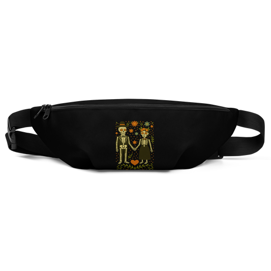 This is a black waist bag with a Día de los Muertos–style illustration of a male and female skeleton holding hands, surrounded by marigolds, vines, and folk art patterns. The skeletons wear traditional black clothing, the man in a suit and hat, the woman with a floral crown with a red heart and leaves at the bottom and the text Creepy All Year. Rendered in warm tones of orange, green, and cream, symbolizing eternal love and remembrance