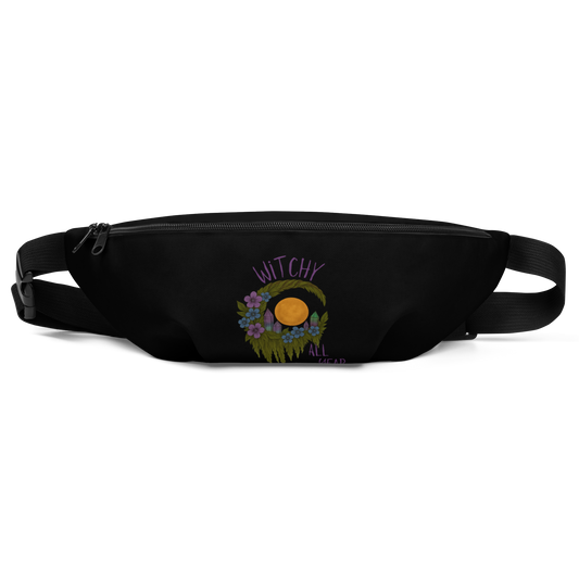 This is a black waist bag fanny pack with a design of a hand-drawn wreath made of moss-covered branches wraps around a glowing sun. The wreath is decorated with purple and blue flowers, small amethyst and fluorite crystals, and strands of hanging moss. The words “Witchy” curve above the wreath and “All Year” sits on the bottom right 