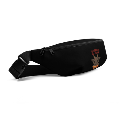 This is a side view of a black waist bag fanny pack that has a cartoon illustration of a baby Baphomet goat with curved horns and a playful grin, wearing bright floral swim trunks while floating in a colorful inner tube. The character is set against a light background with the bold text “Horror All Year” above in red letters 
