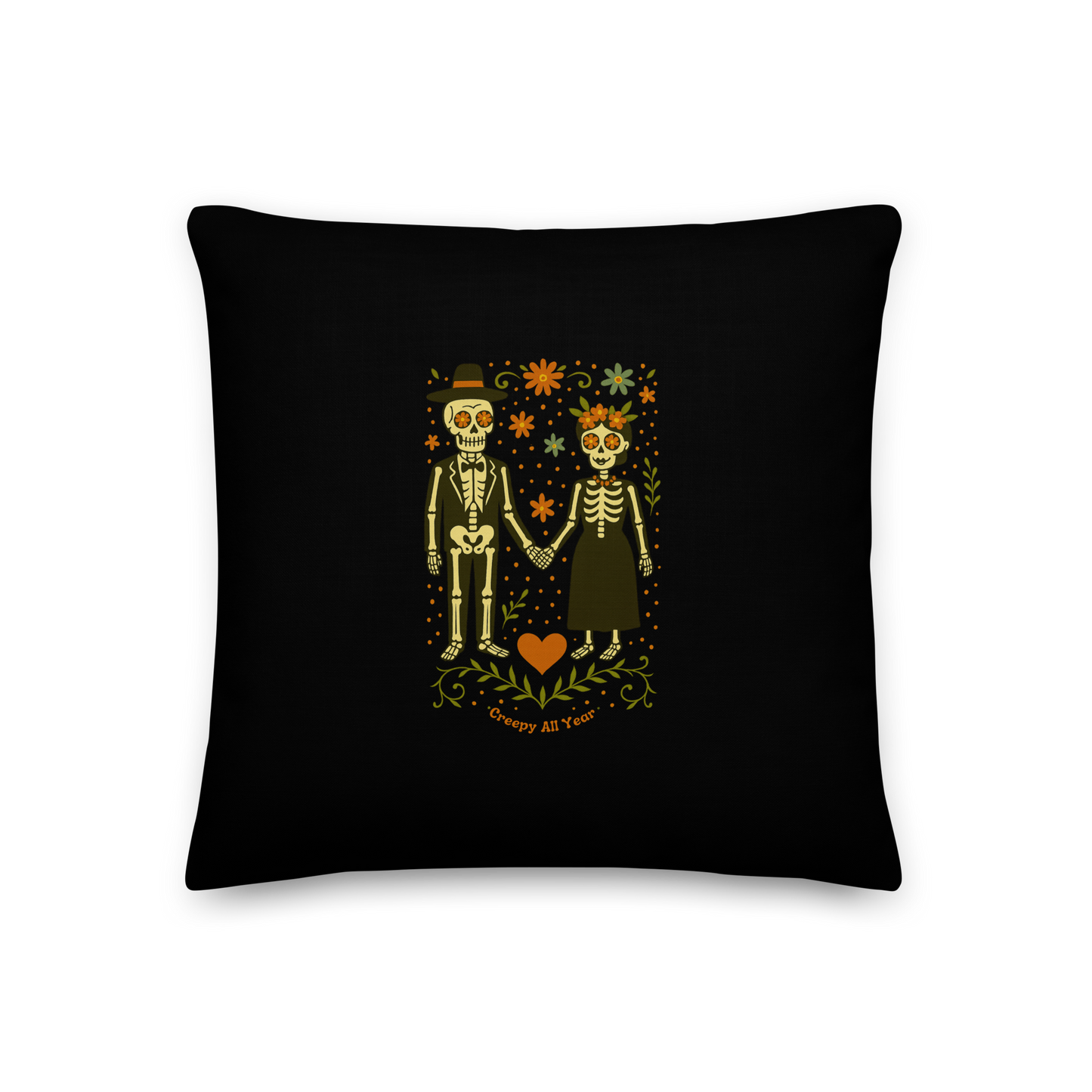 This is a black throw pillow with a Día de los Muertos–style illustration of a male and female skeleton holding hands, surrounded by marigolds, vines, and folk art patterns. The skeletons wear traditional black clothing, the man in a suit and hat, the woman with a floral crown with a red heart and leaves at the bottom and the text Creepy All Year. Rendered in warm tones of orange, green, and cream, symbolizing eternal love and remembrance 