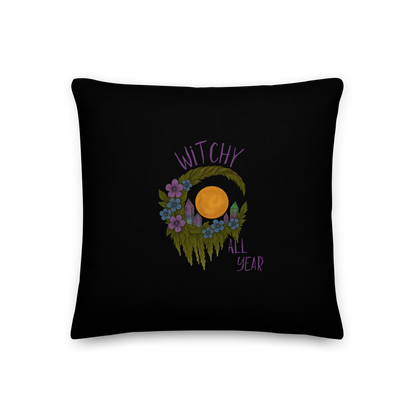 This is black throw pillow with a design of a hand-drawn wreath made of moss-covered branches wraps around a glowing sun. The wreath is decorated with purple and blue flowers, small amethyst and fluorite crystals, and strands of hanging moss. The words “Witchy” curve above the wreath and “All Year” sits on the bottom right 