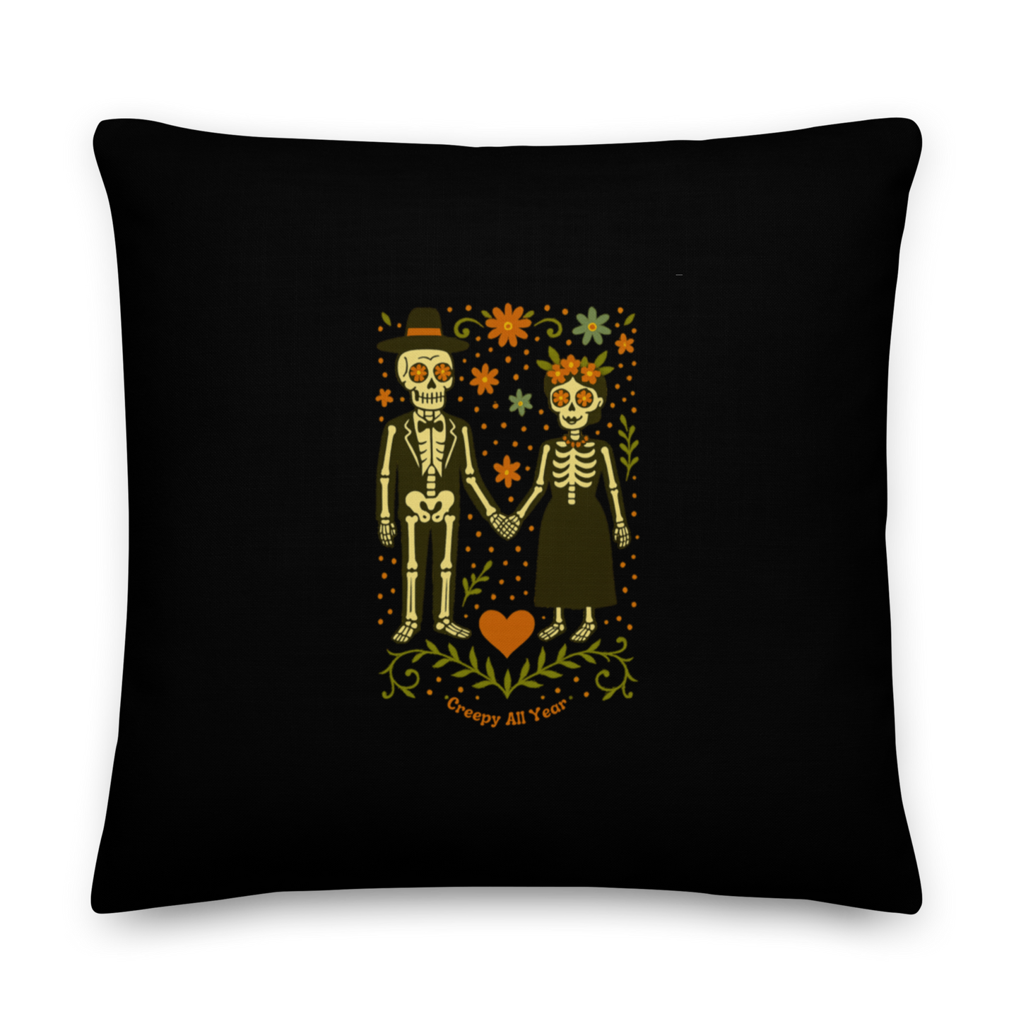 This is a black throw pillow with a Día de los Muertos–style illustration of a male and female skeleton holding hands, surrounded by marigolds, vines, and folk art patterns. The skeletons wear traditional black clothing, the man in a suit and hat, the woman with a floral crown with a red heart and leaves at the bottom and the text Creepy All Year. Rendered in warm tones of orange, green, and cream, symbolizing eternal love and remembrance 