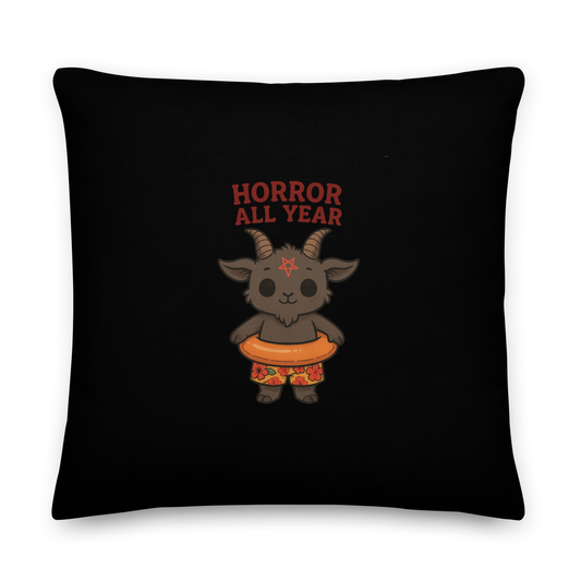 This is a black throw pillow and on the front has a cartoon illustration of a baby Baphomet goat with curved horns and a playful grin, wearing bright floral swim trunks while floating in a colorful inner tube. The character is set against a light background with the bold text “Horror All Year” above in red letters