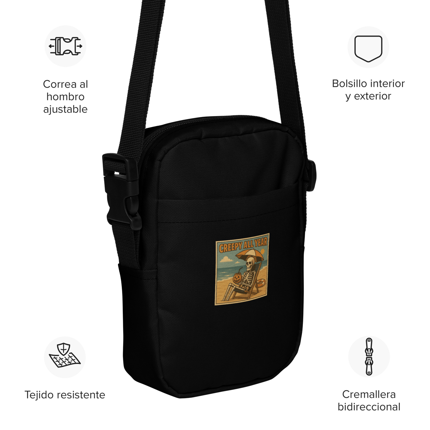This is a black crossbody bag with a retro-style illustration of a grinning skeleton lounging on a beach chair under an orange umbrella. The skeleton is holding a pumpkin-shaped drink cup with a straw and relaxing by the ocean, with a bright sun in the sky and a life preserver in the sand. The words “Creepy All Year” appear boldly at the top 
