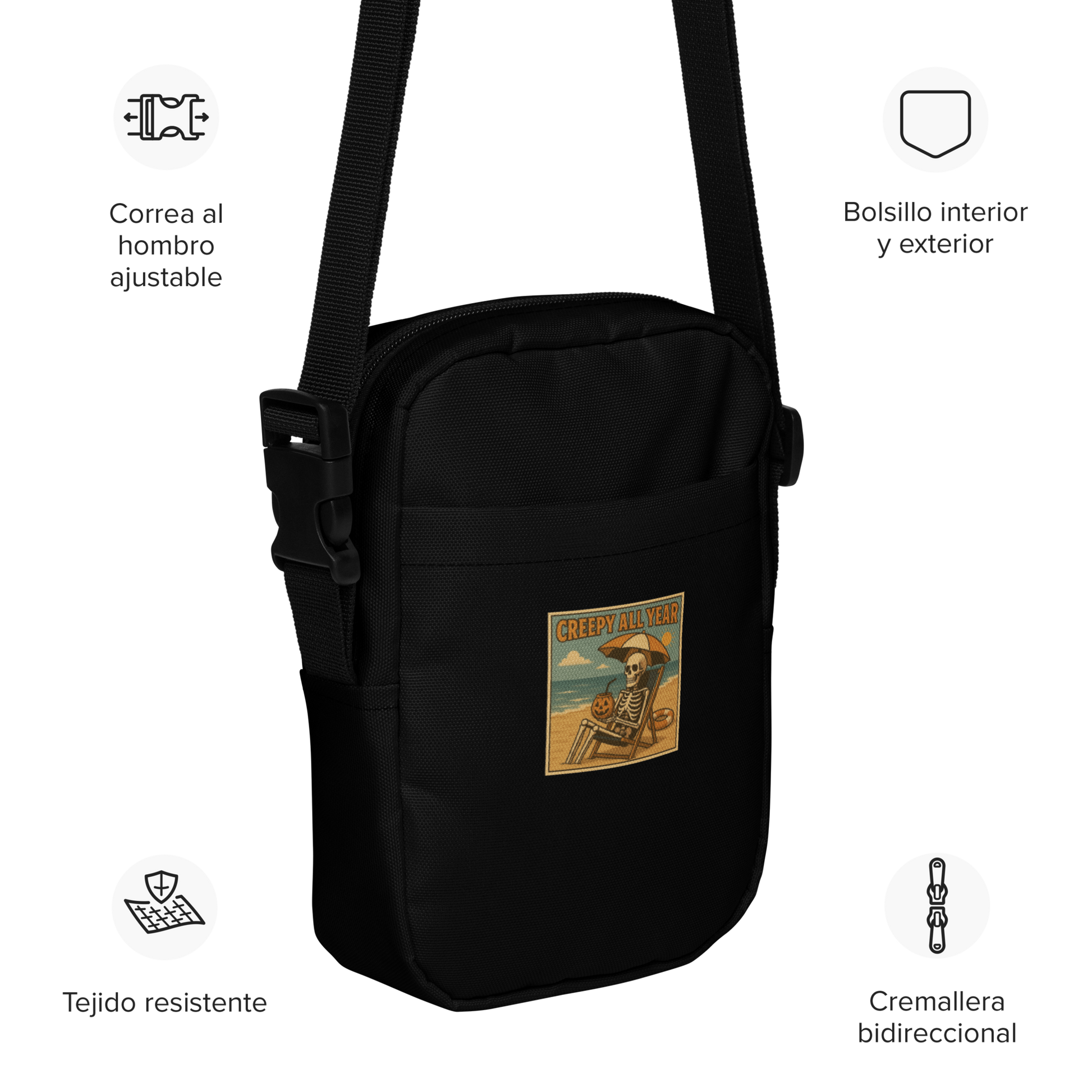 This is a black crossbody bag with a retro-style illustration of a grinning skeleton lounging on a beach chair under an orange umbrella. The skeleton is holding a pumpkin-shaped drink cup with a straw and relaxing by the ocean, with a bright sun in the sky and a life preserver in the sand. The words “Creepy All Year” appear boldly at the top 