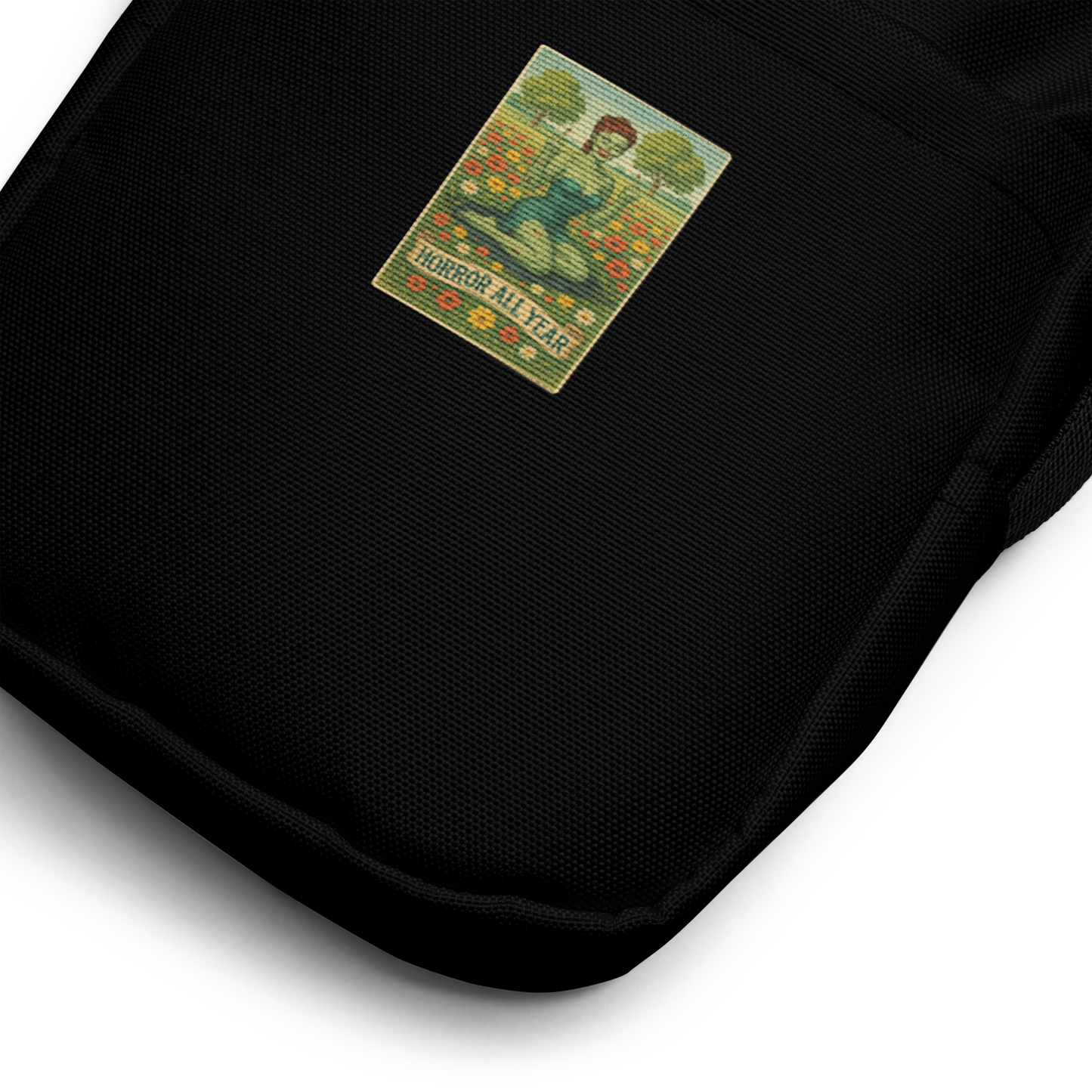 This is a zoom in of a black crossbody bag with a design illustration of a sassy zombie pinup girl standing in a floral field, wearing tattered lingerie and flipping off the viewer with both hands. She has green skin, vintage curls, and a bold attitude. The design blends horror and humor, with a pastel color palette and creepy cute vibes