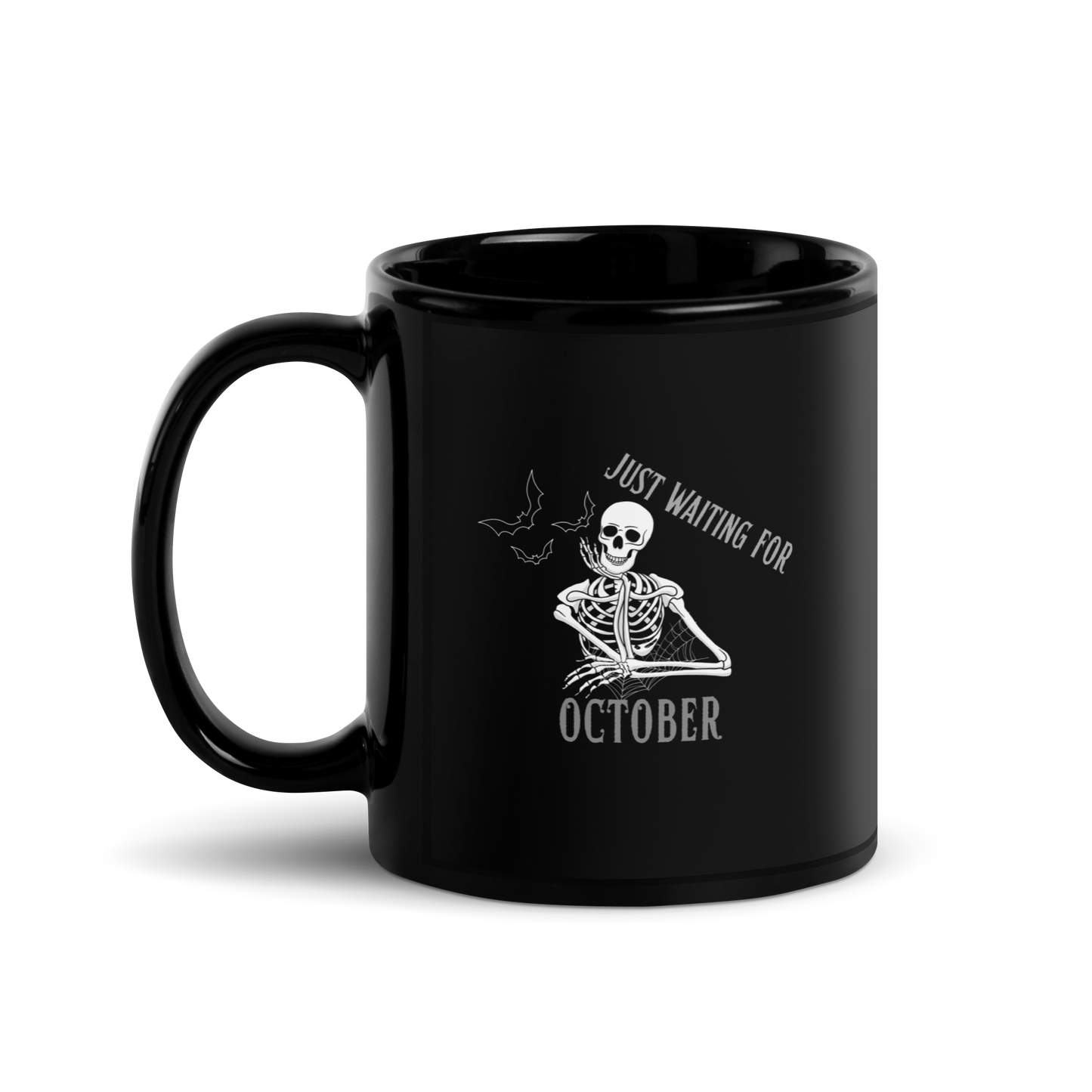 This is a black mug that has a bored skeleton with his head resting in his hand and he has spider webs and bats around him and the text reads just waiting for October