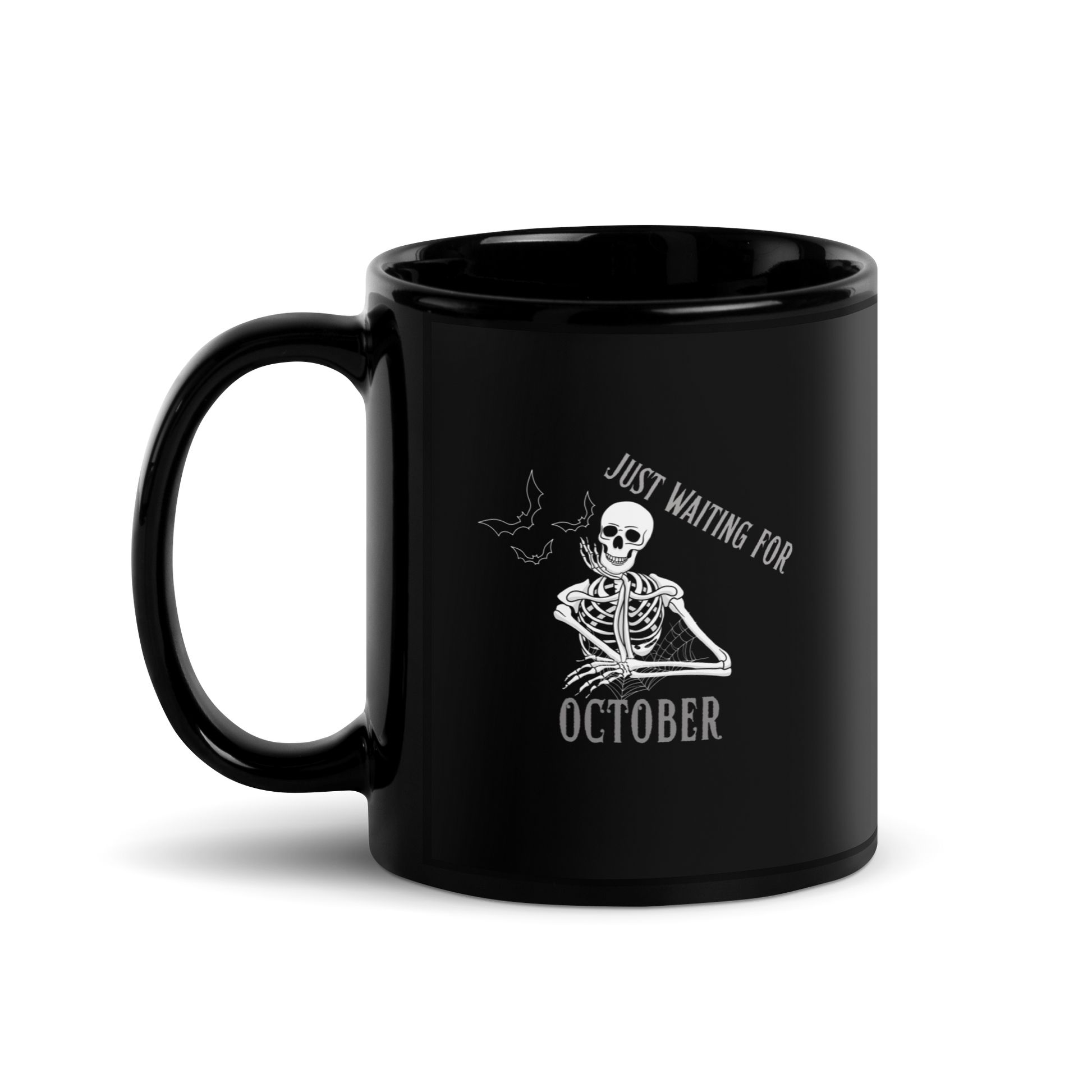 This is a black mug that has a bored skeleton with his head resting in his hand and he has spider webs and bats around him and the text reads just waiting for October