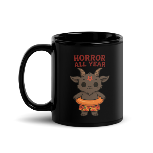 This is a black glossy mug with a cartoon illustration of a baby Baphomet goat with curved horns and a playful grin, wearing bright floral swim trunks while floating in a colorful inner tube. The character is set against a light background with the bold text “Horror All Year” above in red letters 