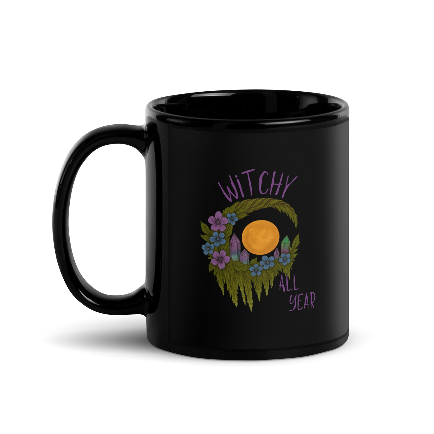 This is a black glossy mug with a design of a hand-drawn wreath made of moss-covered branches wraps around a glowing sun. The wreath is decorated with purple and blue flowers, small amethyst and fluorite crystals, and strands of hanging moss. The words “Witchy” curve above the wreath and “All Year” sits on the bottom right  