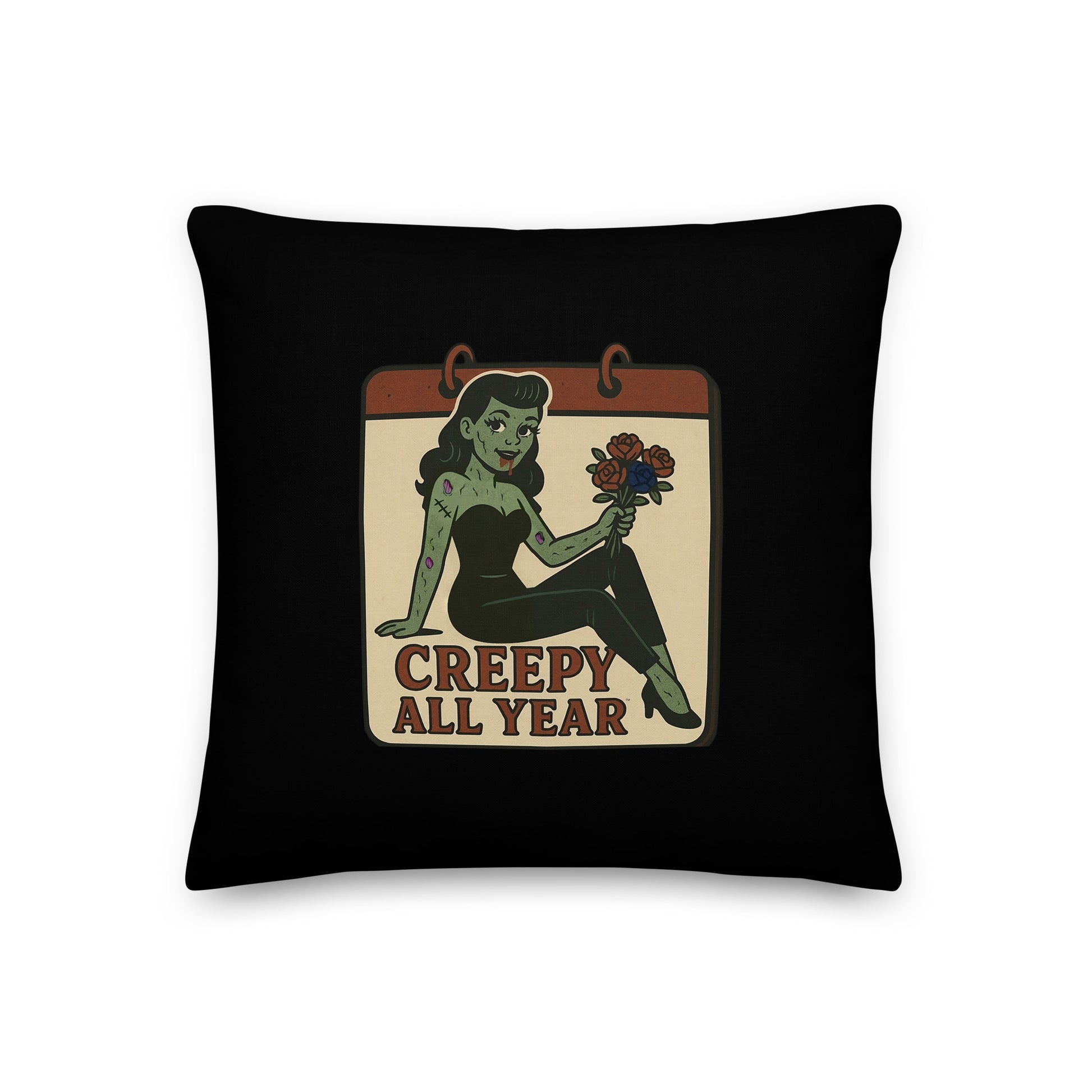 A black pillow with a small vintage-style design. The design features a green pinup-style zombie girl holding flowers, with a banner underneath that reads “CREEPY ALL YEAR.”