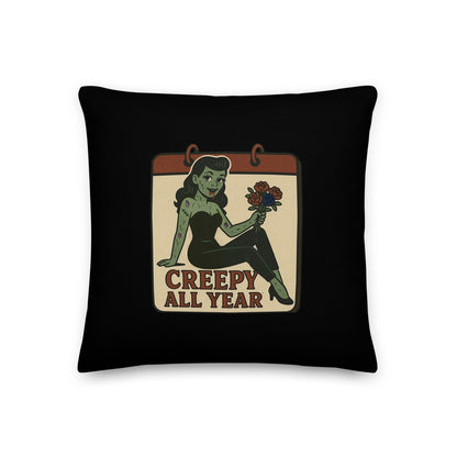 A black pillow with a small vintage-style design. The design features a green pinup-style zombie girl holding flowers, with a banner underneath that reads “CREEPY ALL YEAR.”