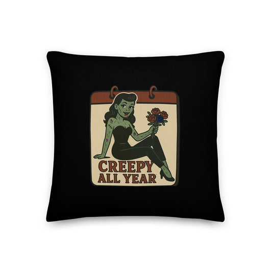 A black pillow with a small vintage-style design. The design features a green pinup-style zombie girl holding flowers, with a banner underneath that reads “CREEPY ALL YEAR.”