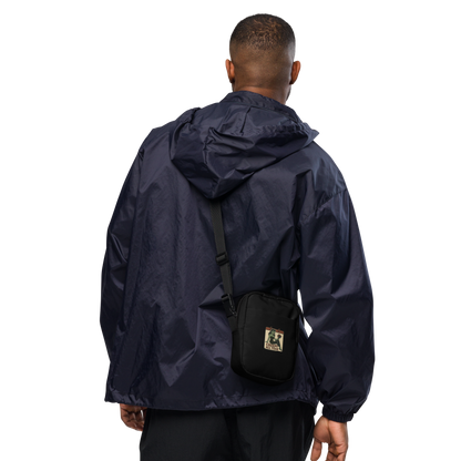 Person wearing a navy raincoat with a black crossbody bag on a white background. The design features a green pinup-style zombie girl holding flowers, with a banner underneath that reads “CREEPY ALL YEAR.”