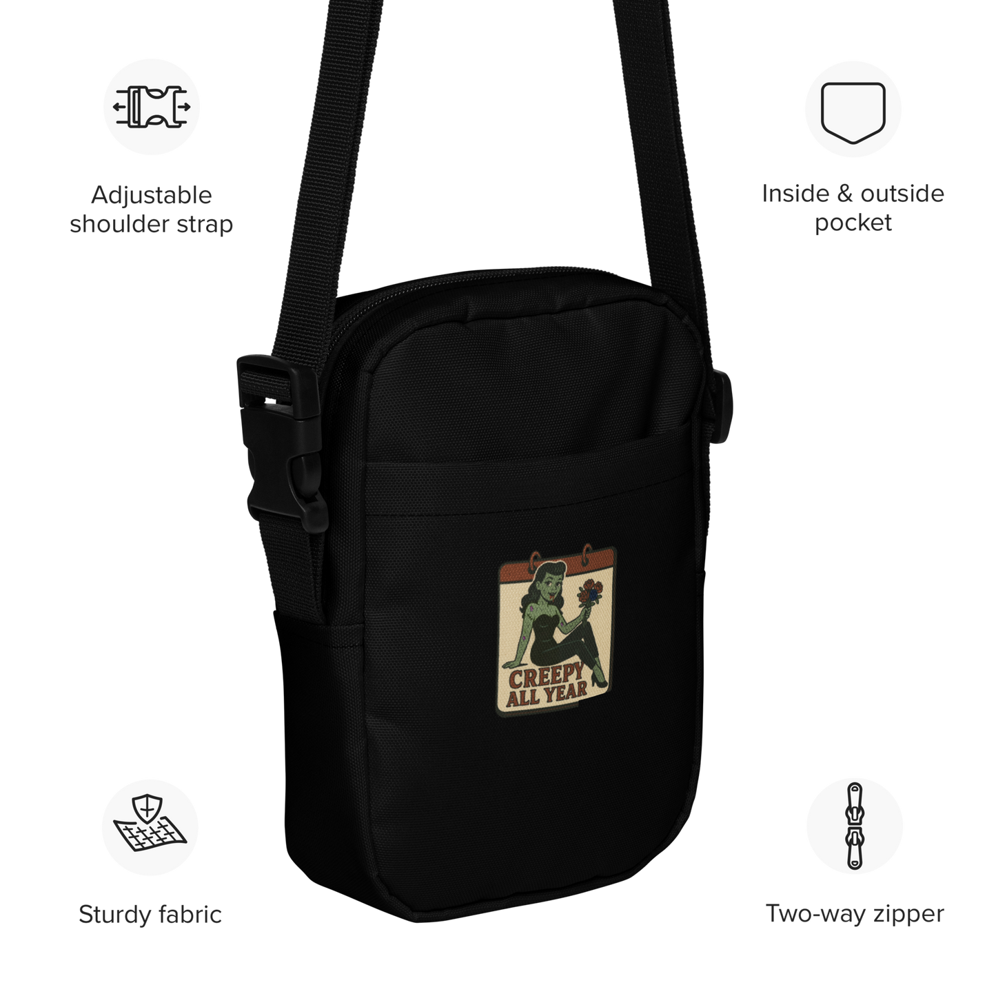 Black bag with a graphic design featuring icons and text describing features. The design features a green pinup-style zombie girl holding flowers, with a banner underneath that reads “CREEPY ALL YEAR.”