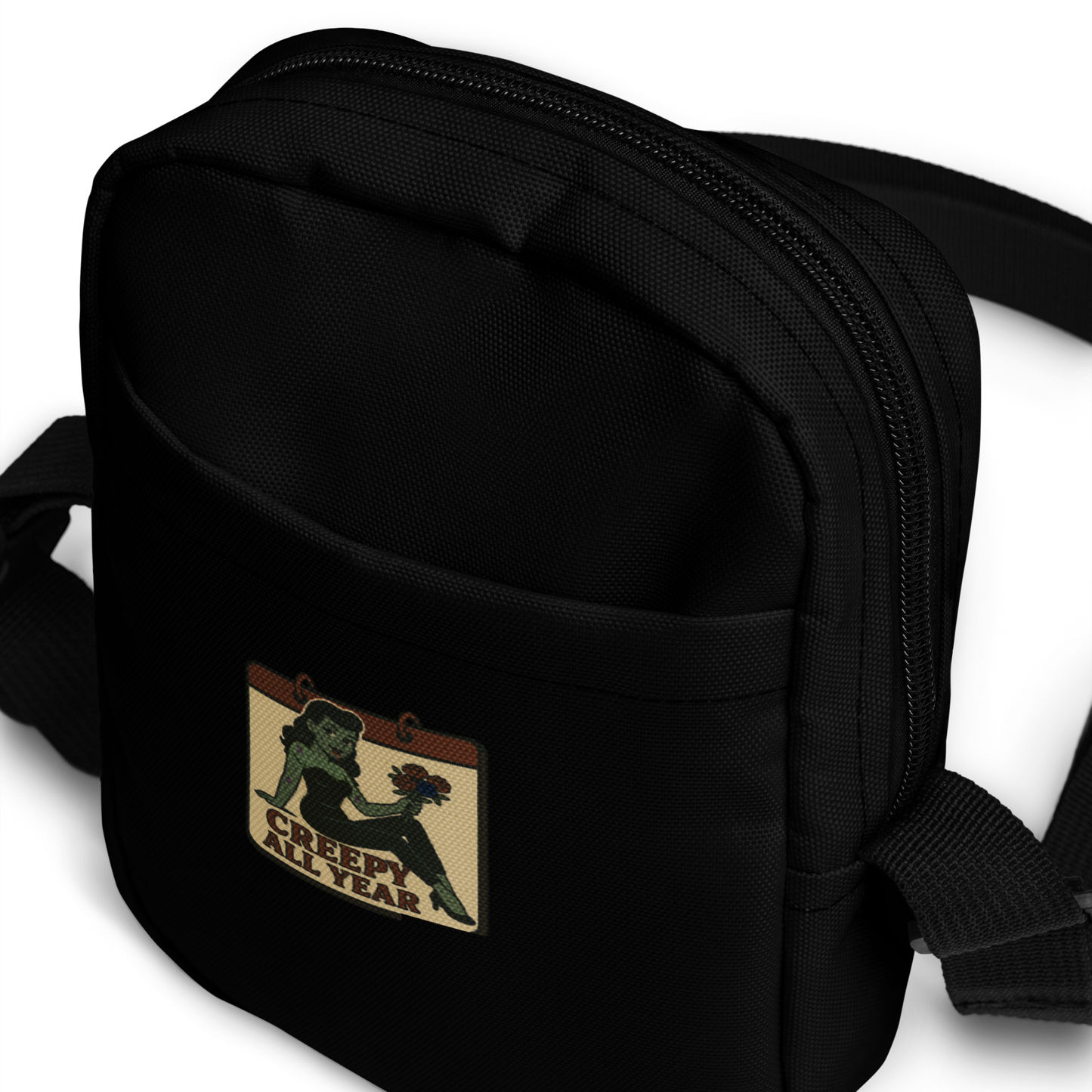Black crossbody bag with a patch featuring a green pinup zombie with the text Creepy All Year