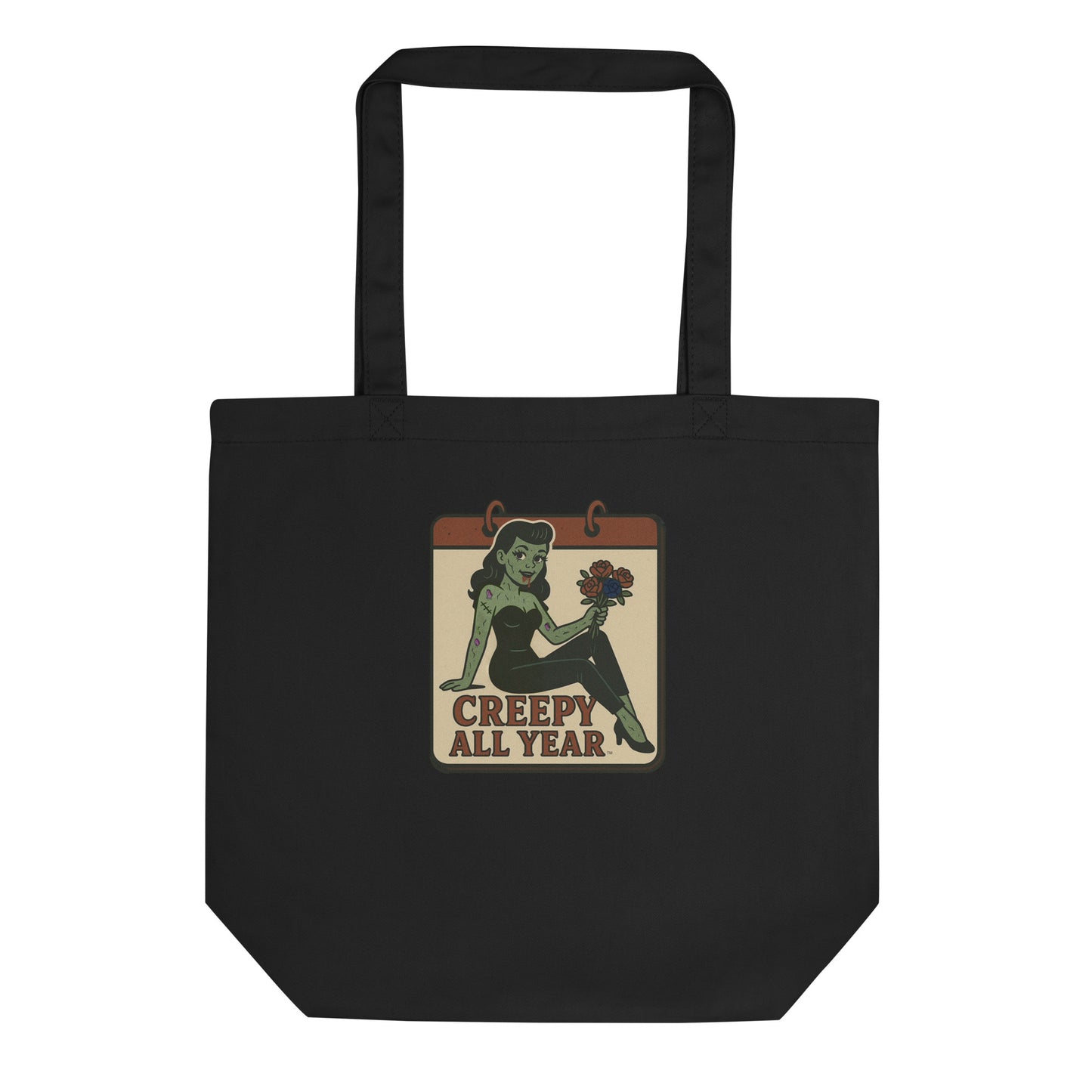 A black tote with a vintage-style design. The design features a green pinup-style zombie girl holding flowers, with a banner underneath that reads “CREEPY ALL YEAR.”