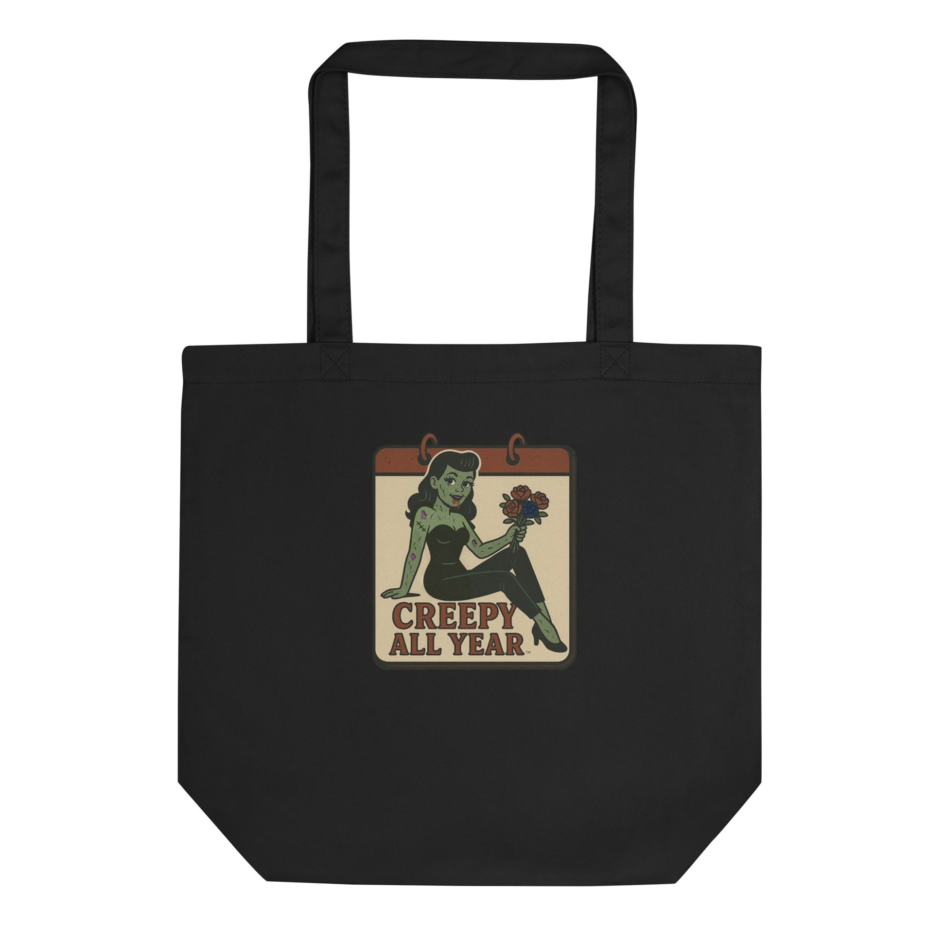 A black tote with a vintage-style design. The design features a green pinup-style zombie girl holding flowers, with a banner underneath that reads “CREEPY ALL YEAR.”