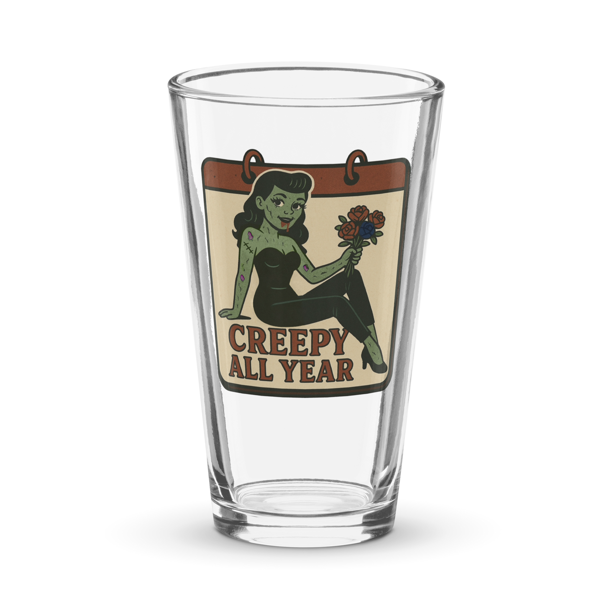 Pint glass with a graphic design. The design features a green pinup-style zombie girl holding flowers, with a banner underneath that reads “CREEPY ALL YEAR.”