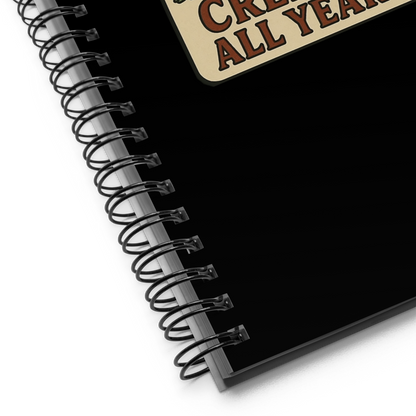 Black spiral-bound notebook with a decorative corner label on a white background. The design has a banner underneath that reads “CREEPY ALL YEAR.”

