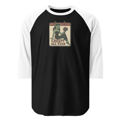 A black and white raglan t-shirt with a small vintage-style design. The design features a green pinup-style zombie girl holding flowers, with a banner underneath that reads “CREEPY ALL YEAR.”