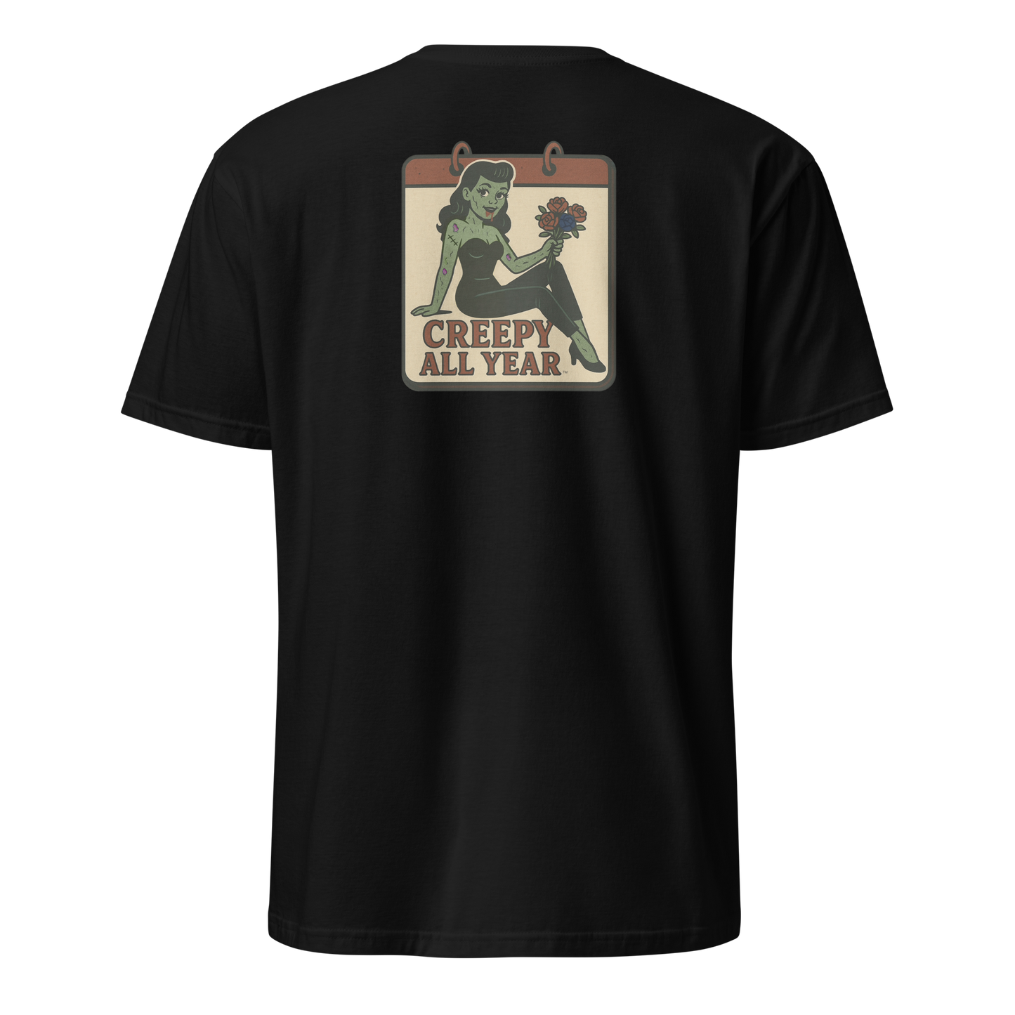 A black t-shirt with a vintage-style design on the back area. The design features a green pinup-style zombie girl holding flowers, with a banner underneath that reads “CREEPY ALL YEAR.”