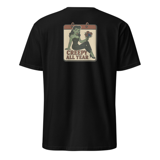 A black t-shirt with a vintage-style design on the back area. The design features a green pinup-style zombie girl holding flowers, with a banner underneath that reads “CREEPY ALL YEAR.”