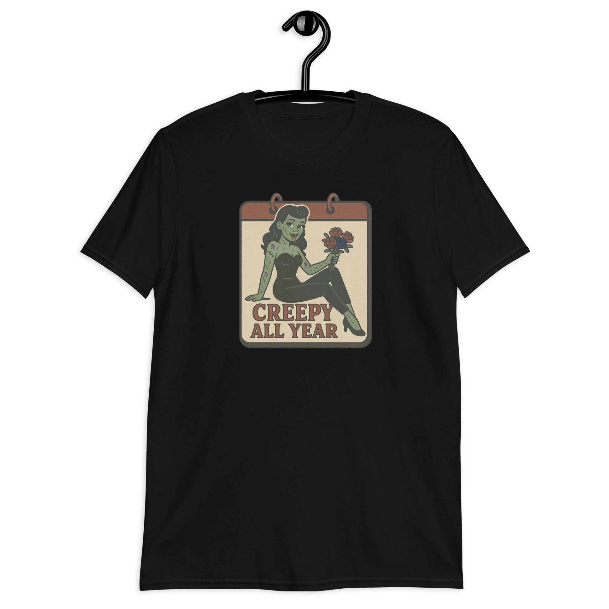 A black t-shirt on a hanger with a vintage-style design on the front. The design features a green pinup-style zombie girl holding flowers, with a banner underneath that reads “CREEPY ALL YEAR.”