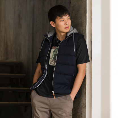 A man indoors standing in front of stairs with black hair wearing cargo pants and t-shirt with vintage style design. The design on the front features a green pinup-style zombie girl holding flowers, with a banner underneath that reads “CREEPY ALL YEAR.”