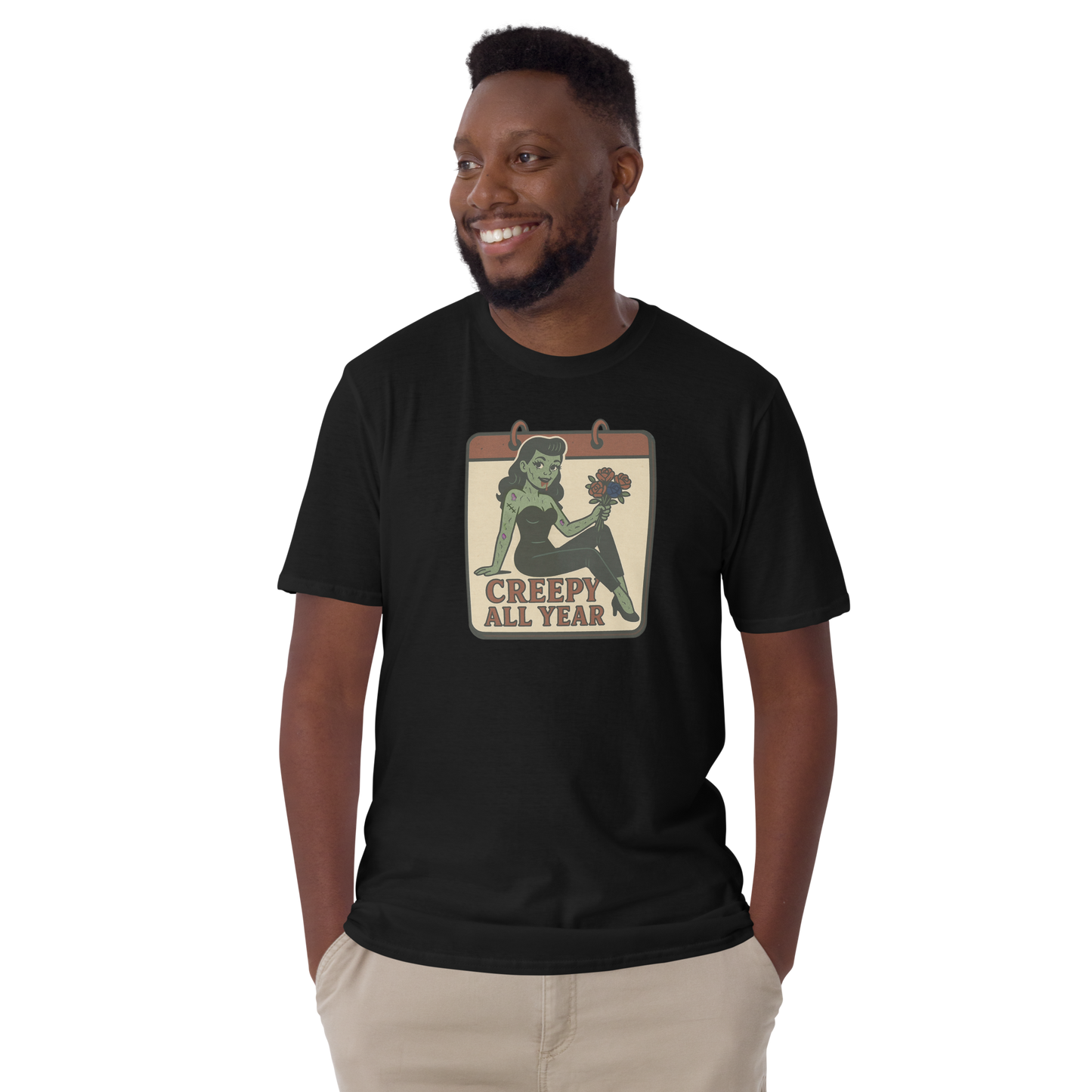 A t-shirt on a man with short balck hair with a vintage-style design on the front. The design features a green pinup-style zombie girl holding flowers, with a banner underneath that reads “CREEPY ALL YEAR.”