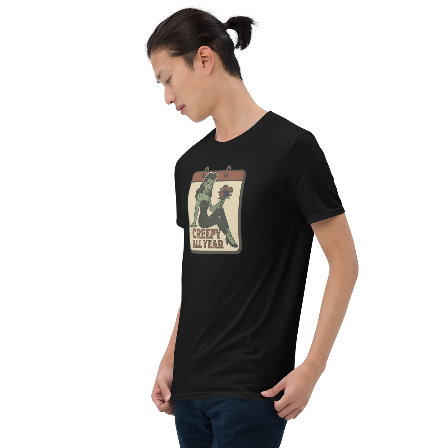 A guy with black hair wearing jeans and t-shirt with vintage style design. The design on the front features a green pinup-style zombie girl holding flowers, with a banner underneath that reads “CREEPY ALL YEAR.”
