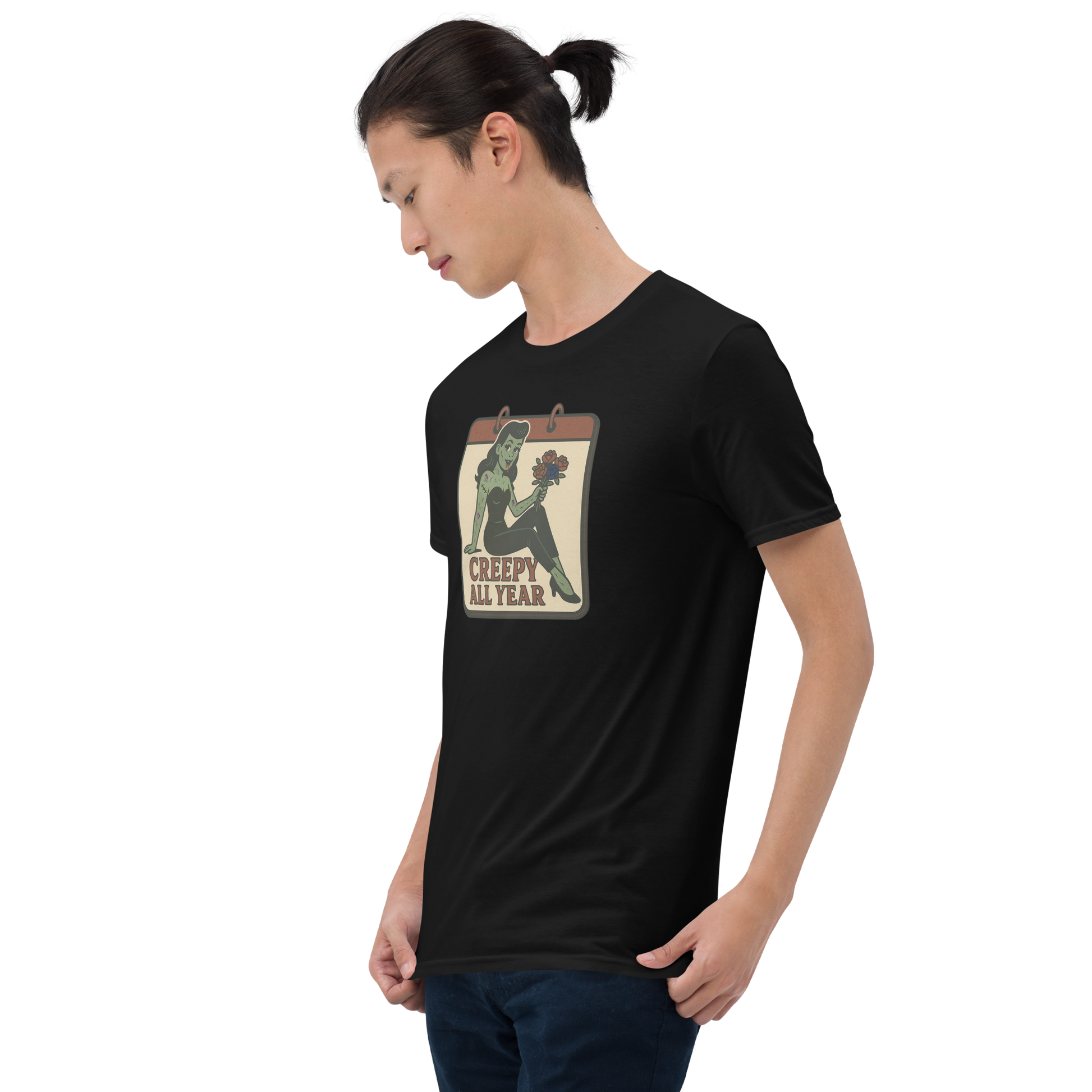 A guy with black hair wearing jeans and t-shirt with vintage style design. The design on the front features a green pinup-style zombie girl holding flowers, with a banner underneath that reads “CREEPY ALL YEAR.”
