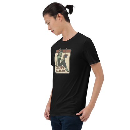 A guy with black hair wearing jeans and t-shirt with vintage style design. The design on the front features a green pinup-style zombie girl holding flowers, with a banner underneath that reads “CREEPY ALL YEAR.”