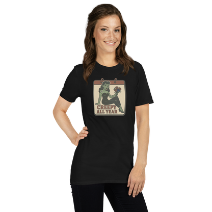 A girl with long brown hair wearing black pants and t-shirt with vintage style design. The design on the front features a green pinup-style zombie girl holding flowers, with a banner underneath that reads “CREEPY ALL YEAR.”