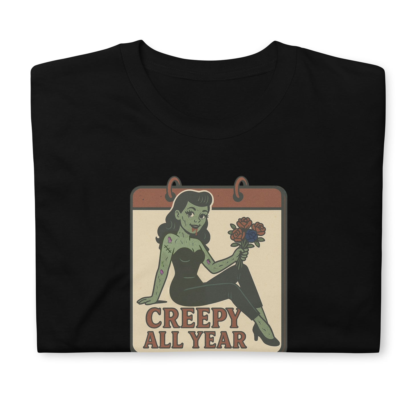 A vintage-style design on the front of a black t-shirt. The design features a green pinup-style zombie girl holding flowers, with a banner underneath that reads “CREEPY ALL YEAR.”