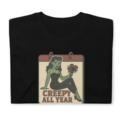 A vintage-style design on the front of a black t-shirt. The design features a green pinup-style zombie girl holding flowers, with a banner underneath that reads “CREEPY ALL YEAR.”