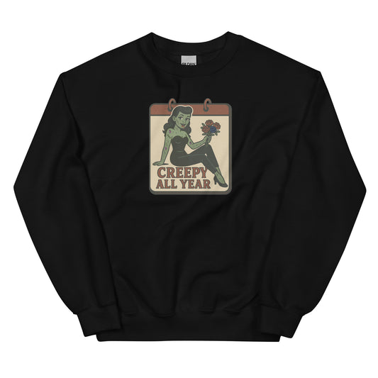 A black sweatshirt with a vintage-style design on the front. The design features a green pinup-style zombie girl holding flowers, with a banner underneath that reads “CREEPY ALL YEAR.”